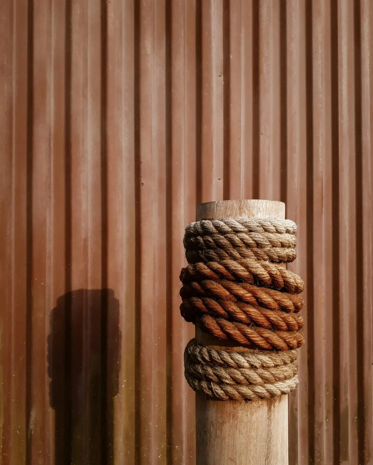 Timber post wrapped in rope against a corrugated wall