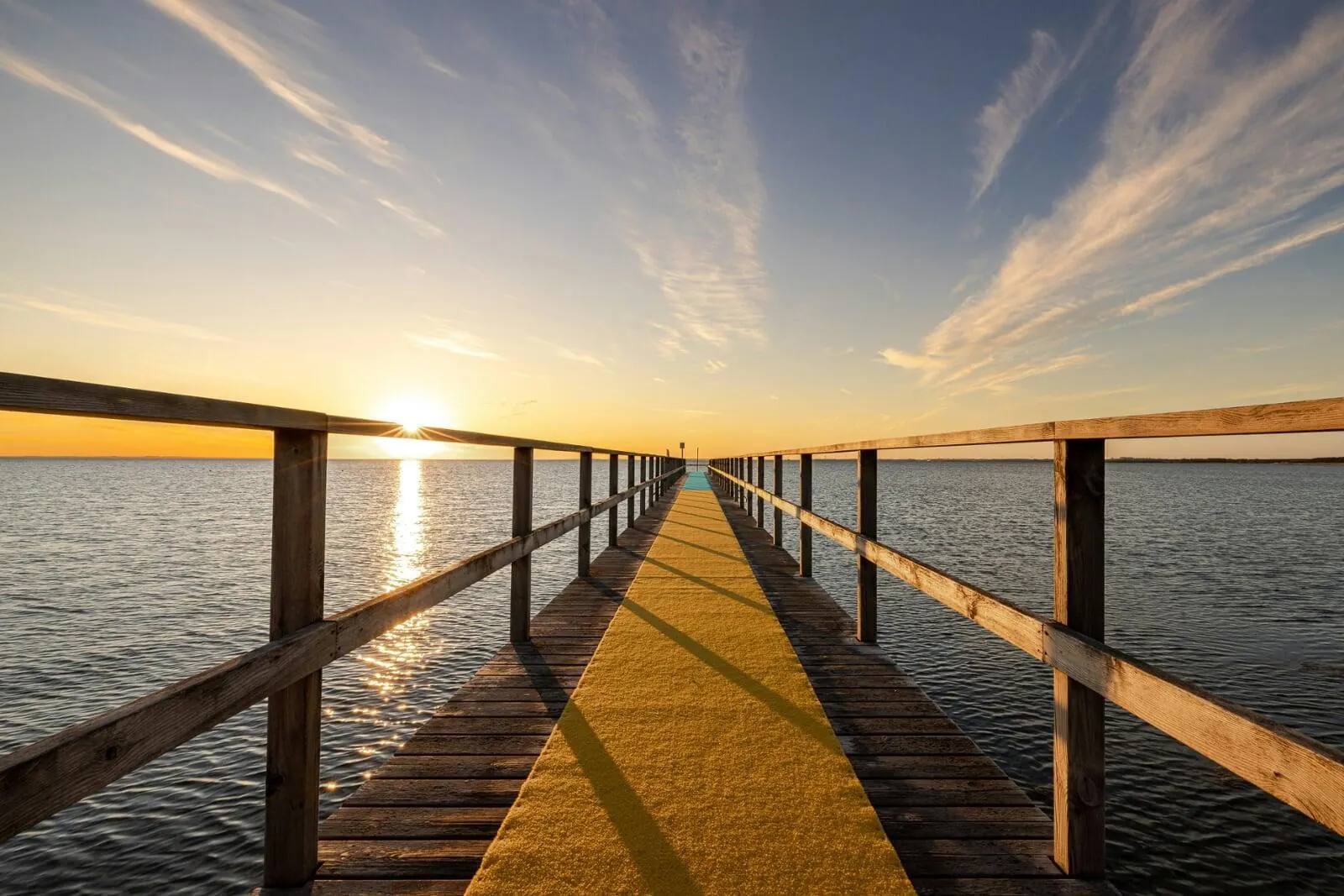 Timber jetty with handrails stretching over calm water at sunset
